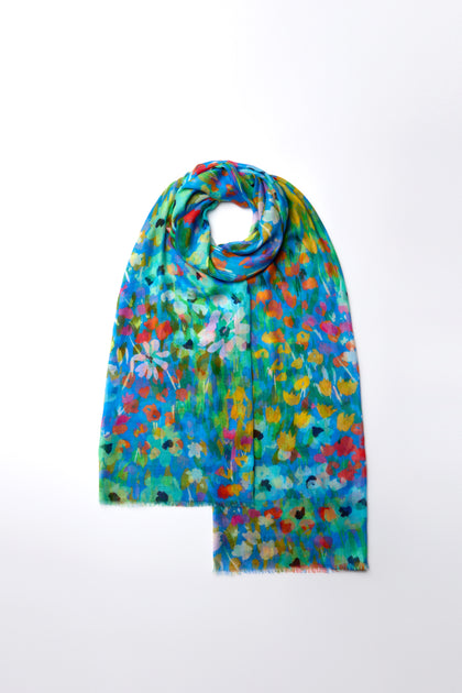 Meet the Abstract Painted Garden Scarf: a lightweight scarf adorned with vivid, multicolored floral patterns set against a calming blue backdrop on a white base.