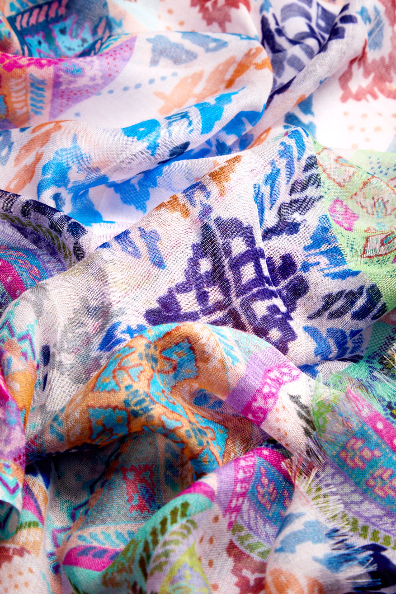 The Soft Graphic Patchwork Scarf, a vibrant statement piece, boasts a colorful, crumpled fabric with intricate geometric and abstract patterns in blue, purple, orange, and green tones. Versatile and timeless, it's perfect for any occasion.