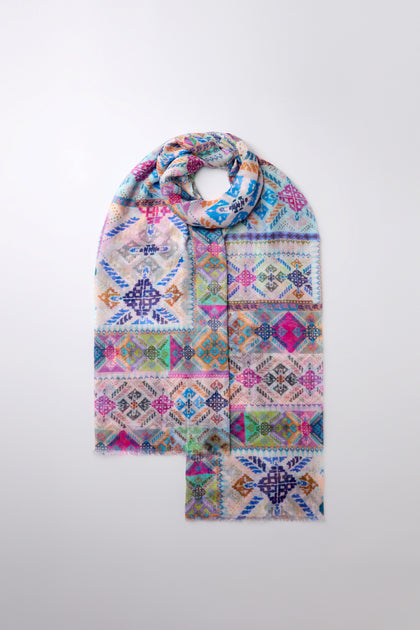 The Soft Graphic Patchwork Scarf features vibrant geometric patterns in blue, pink, green, and purple on a light background. Its versatile design creates an abstract print that pops on a white surface.