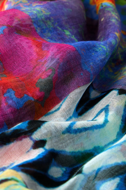 The Sahara Patchwork Scarf showcases a vivid mix of abstract patterns in blue, red, purple, and green on colorful fabric, highlighting its smooth folds and textures.