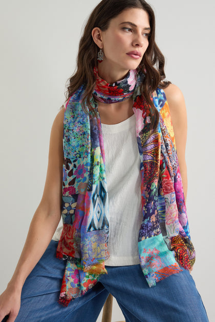 A person wearing the Sahara Patchwork Scarf, which enhances their white top and blue pants, sits against a plain background.