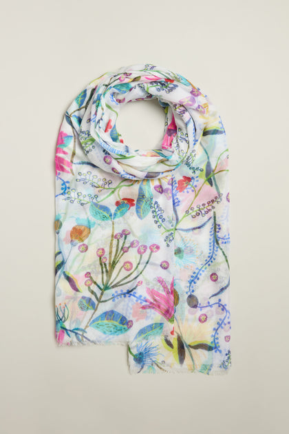 Discover the Wild Garden Scarf, a lightweight accessory with a vibrant floral design. Showcasing various flowers and leaves on a pristine white background, it adds timeless elegance to any wardrobe.