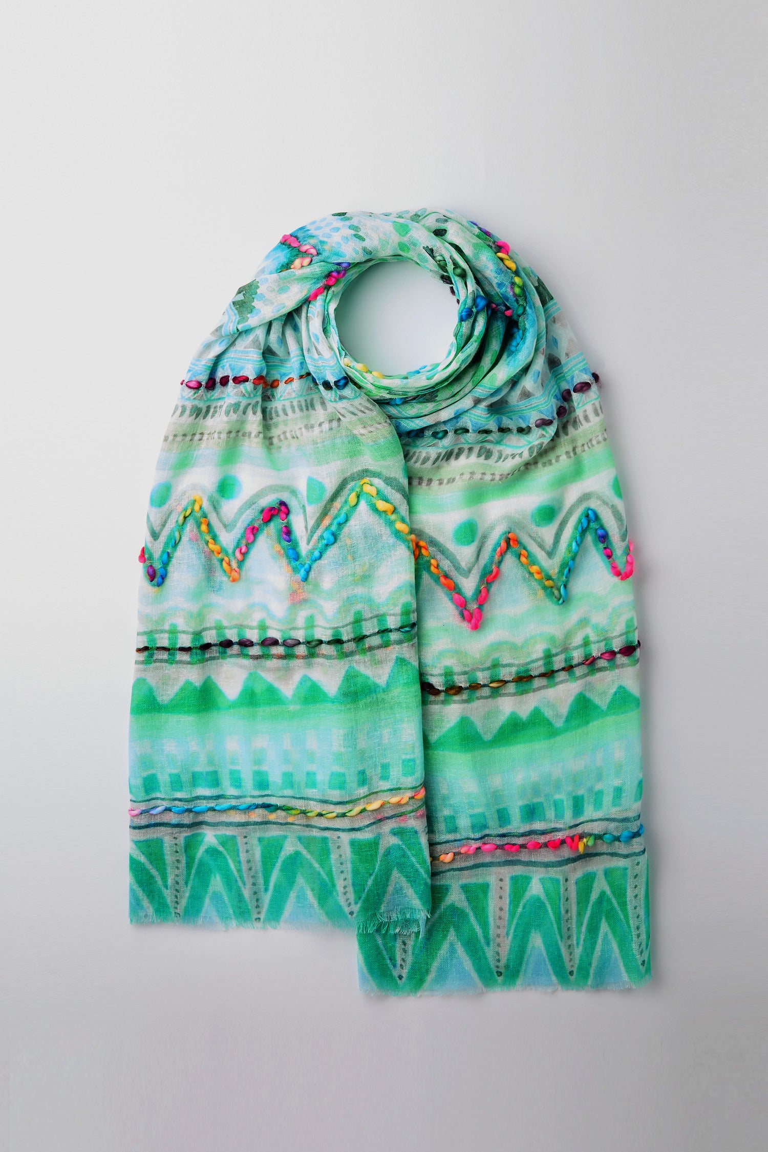 The Embroidered Zig Zag Stitch Scarf in green, featuring multicolored zigzag patterns and geometric designs, is neatly folded on a neutral background and embodies lightweight elegance.