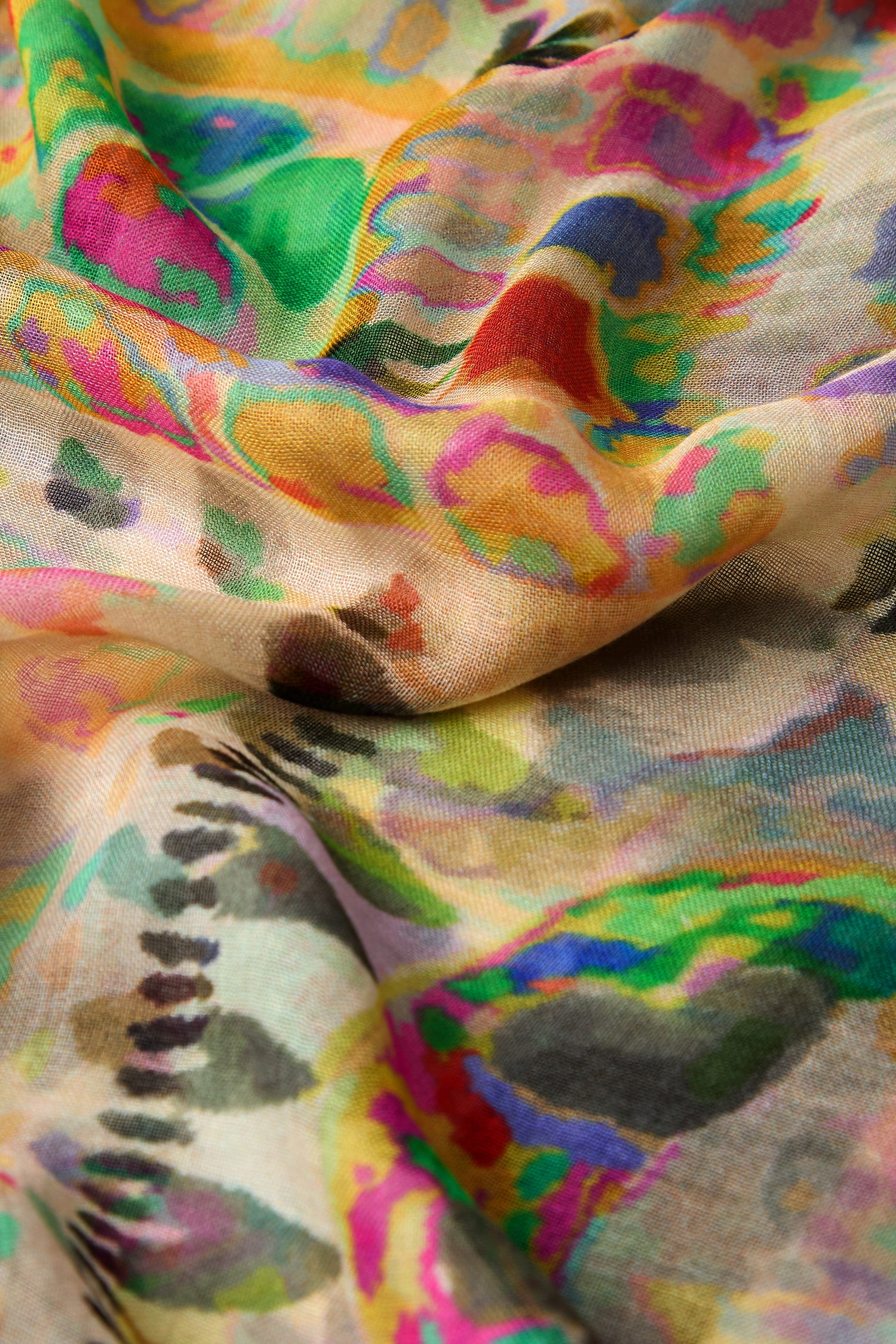 A close-up of a Collage Modal Scarf reveals a vibrant abstract pattern with swirling designs in green, pink, blue, and yellow, reminiscent of an intricate collage print on lightweight fabric.