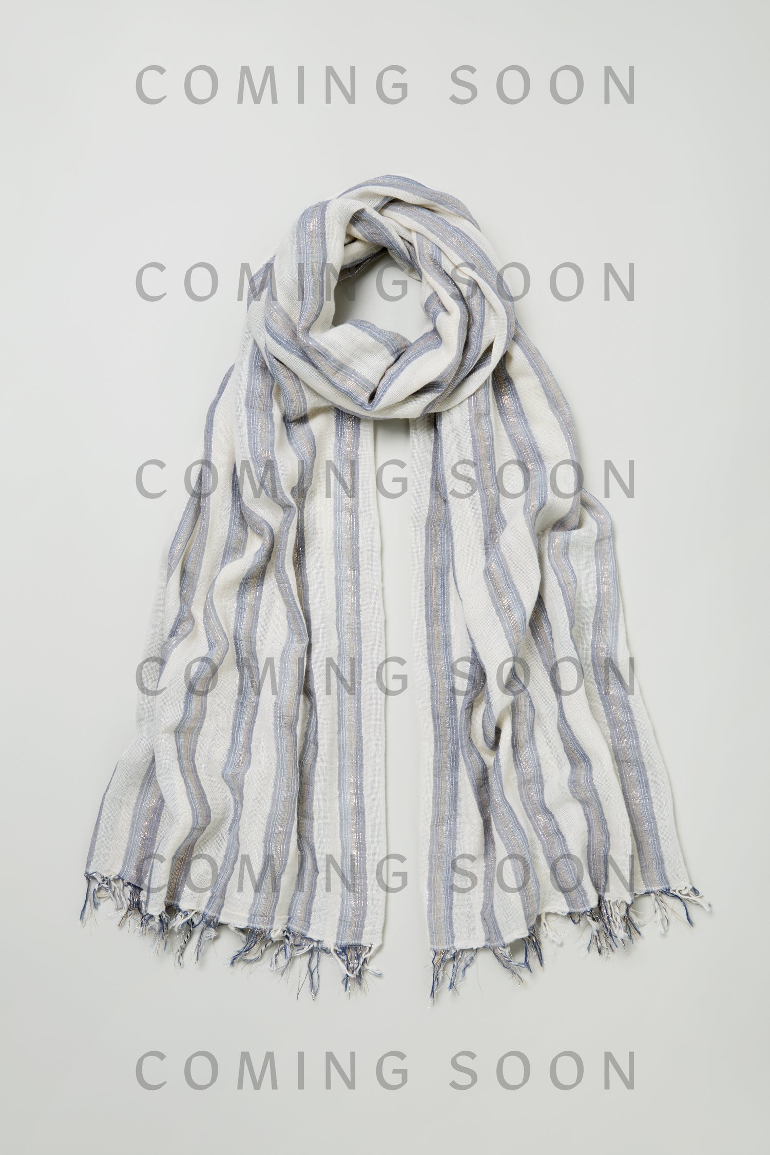 The Lurex Stripe Cotton Blend Scarf, a light-colored scarf with stripes and fringed edges, is displayed flat on a white background with "COMING SOON" in bold gray letters across the image.