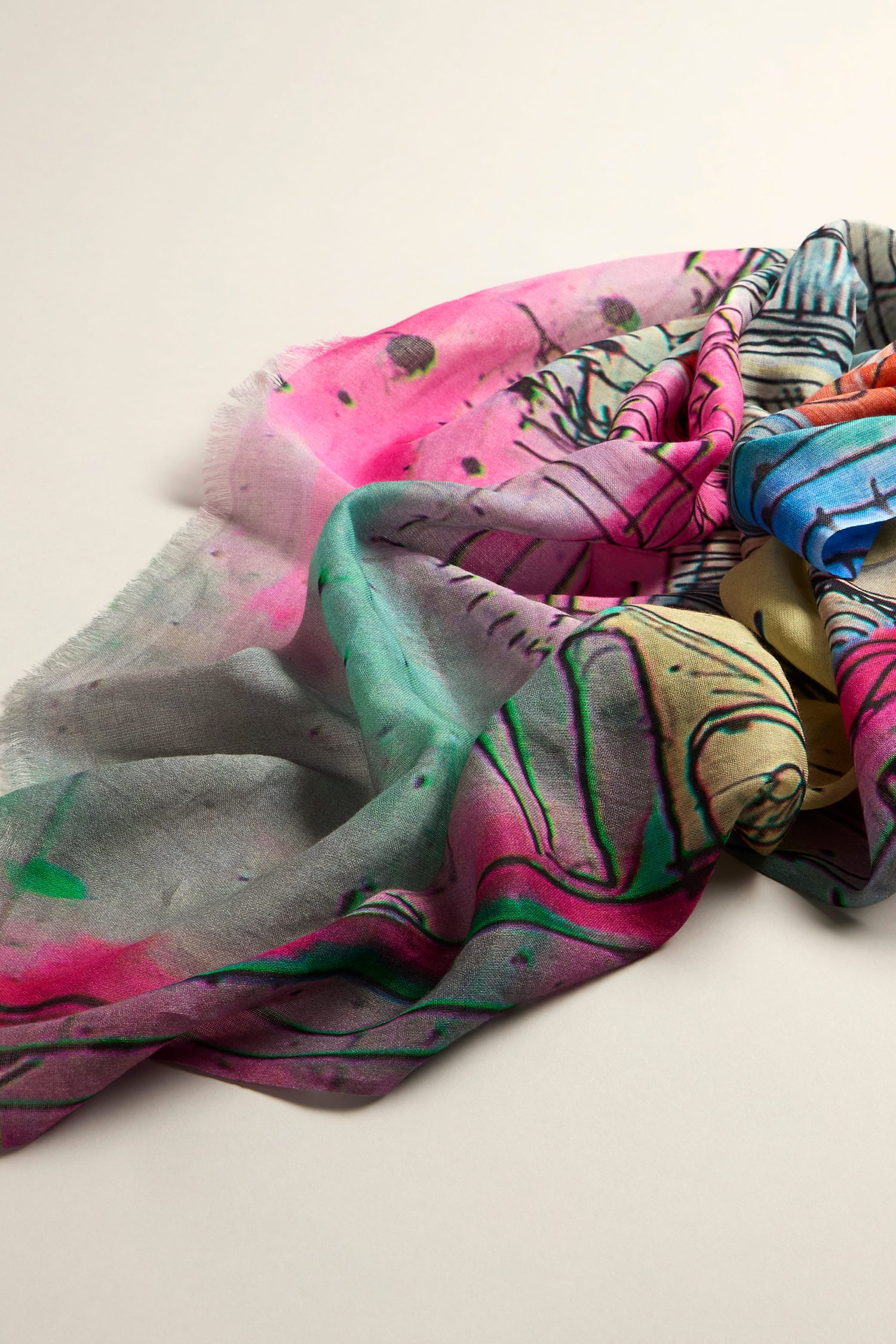 The Abstract City Sketch Cotton Modal Scarf showcases a vibrant blend of abstract patterns in pink, green, blue, and gray hues. Draped elegantly on a flat surface, it exudes dynamic style and modern elegance.