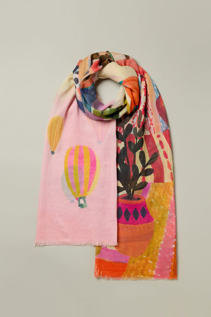 The Marrakech Cotton Modal Scarf vibrantly showcases colorful hot air balloons, abstract shapes, and a potted plant design on a light background, capturing the lively spirit of Moroccan markets and adding an exotic flair to your ensemble.