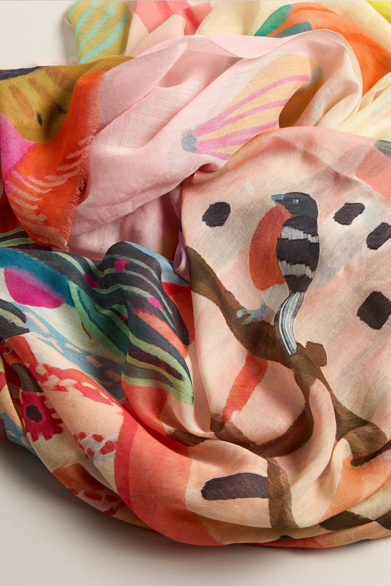 Inspired by Moroccan markets, the Marrakech Cotton Modal Scarf is a vibrant accessory displaying a colorful crumpled design with a bird painting amid abstract pink, orange, and green patterns.