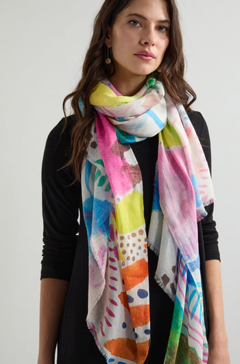 A woman in a black outfit wears the Summit Cotton Modal Scarf, showcasing its colorful pattern gracefully around her neck; the lightweight, breathable scarf adds a touch of elegance.