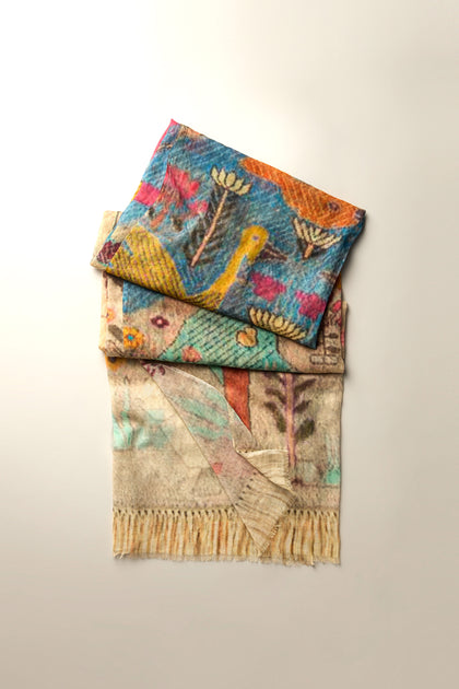 Two Riverside Cotton Mix Scarves feature abstract bird and nature designs, offering lightweight comfort. Available in vibrant and muted tones, these breathable scarves rest gracefully on a light surface.