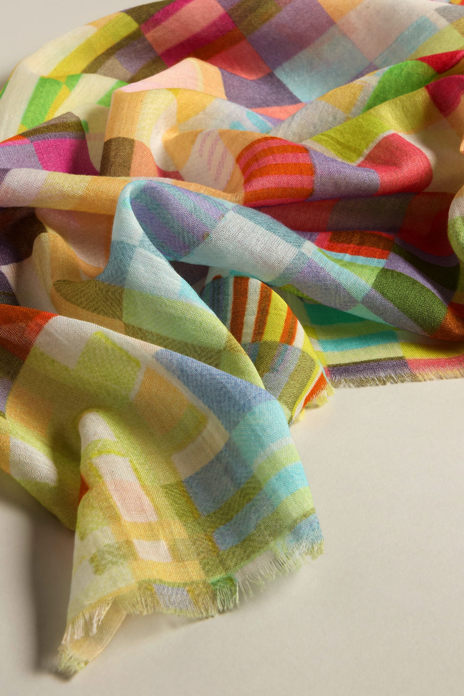 A vibrant fabric featuring stripes and squares in shades of green, yellow, pink, and blue drapes elegantly on beige, resembling the Rainbow Checkerboard Cotton Modal Scarf.