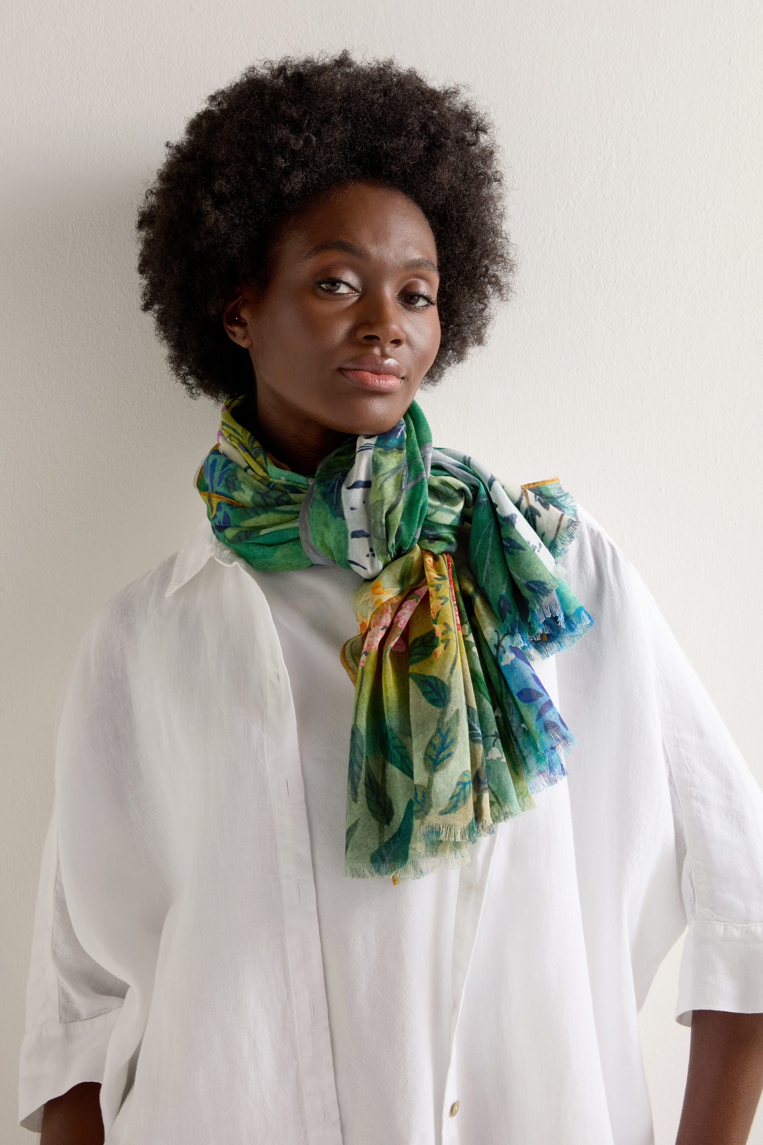 A person in a white shirt wears the lightweight and versatile Painted Garden Cotton Scarf, adorned with vibrant floral designs, standing against a plain background.