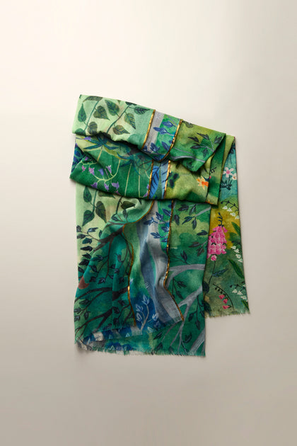 The Painted Garden Cotton Scarf is a lightweight and versatile accessory, showcasing a vibrant floral and leaf pattern against a plain backdrop.