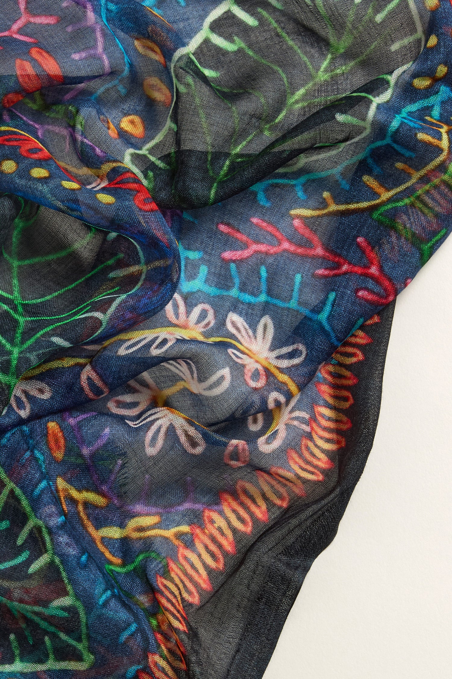 Close-up of a Painted Leaves Modal Scarf made from luxuriously soft modal fabric with vibrant hand-painted leaf prints in blues, greens, reds, and yellows on a dark backdrop.