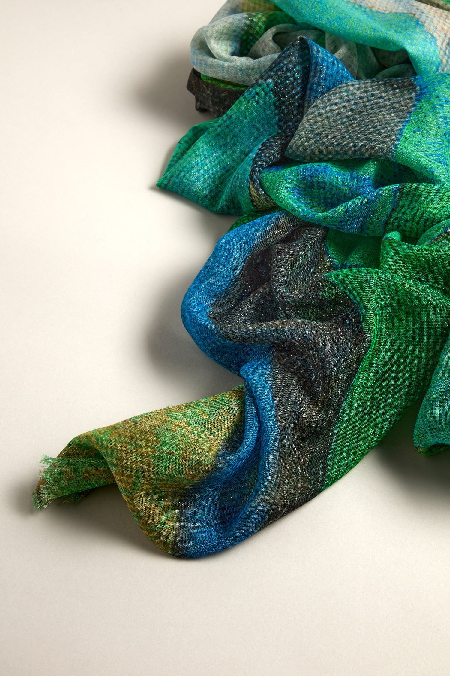 The Tide Sparkle Scarf features a luminous design with its textured fabric in vibrant blue, green, and black on a neutral base.