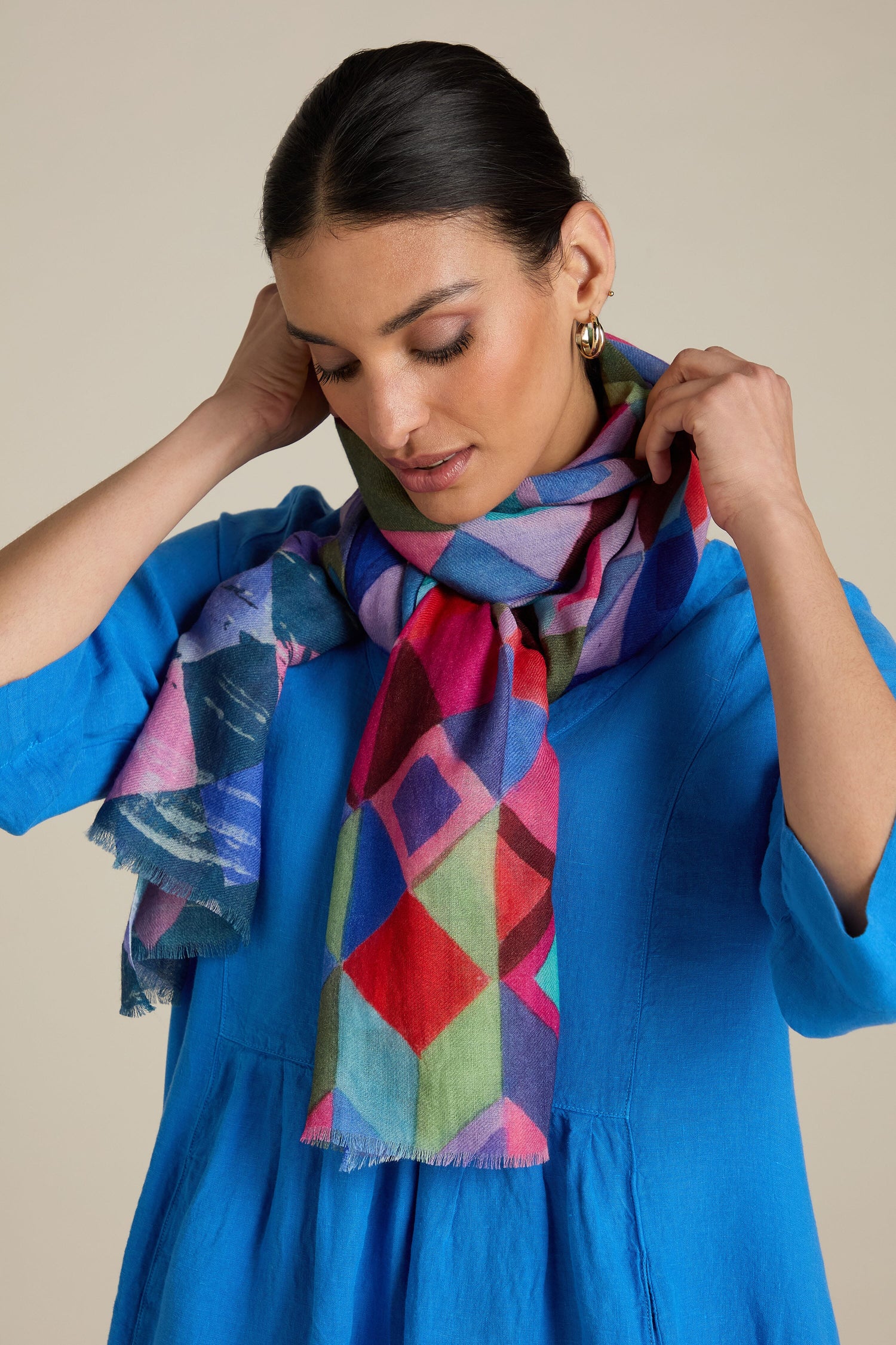 A woman in a blue top adjusts the Painted Squares Wool Mix Scarf with its colorful geometric motif around her neck.