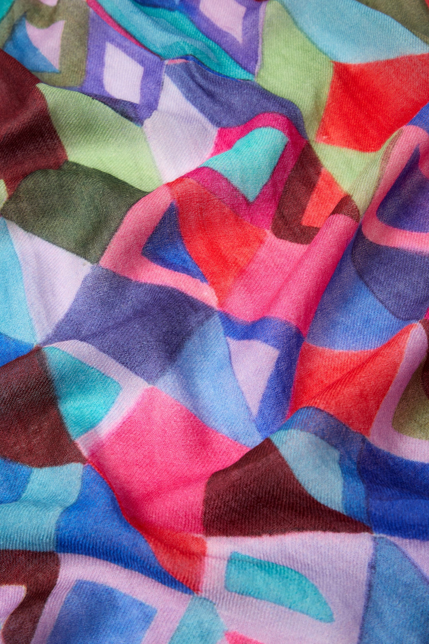 A close-up of the Painted Squares Wool Mix Scarf showcases an accessory decorated with a vibrant, abstract-patterned fabric featuring an array of geometric motifs in shades of pink, blue, red, green, and purple.