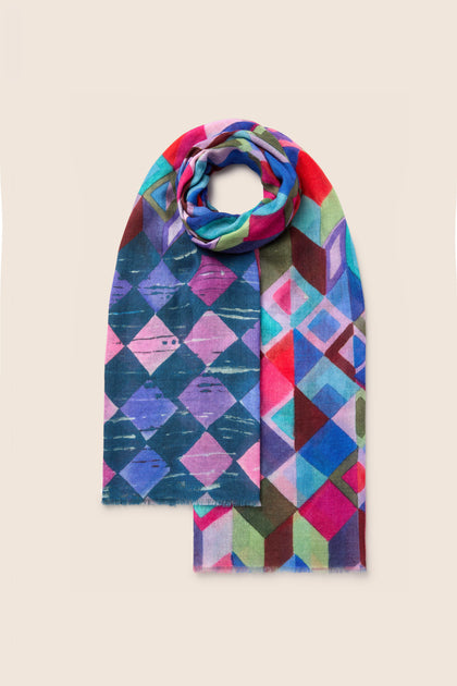 The Painted Squares Wool Mix Scarf is a vibrant accessory that features an abstract geometric motif in shades of blue, pink, green, and red on a beige background. This stylish scarf adds a pop of color to any outfit.