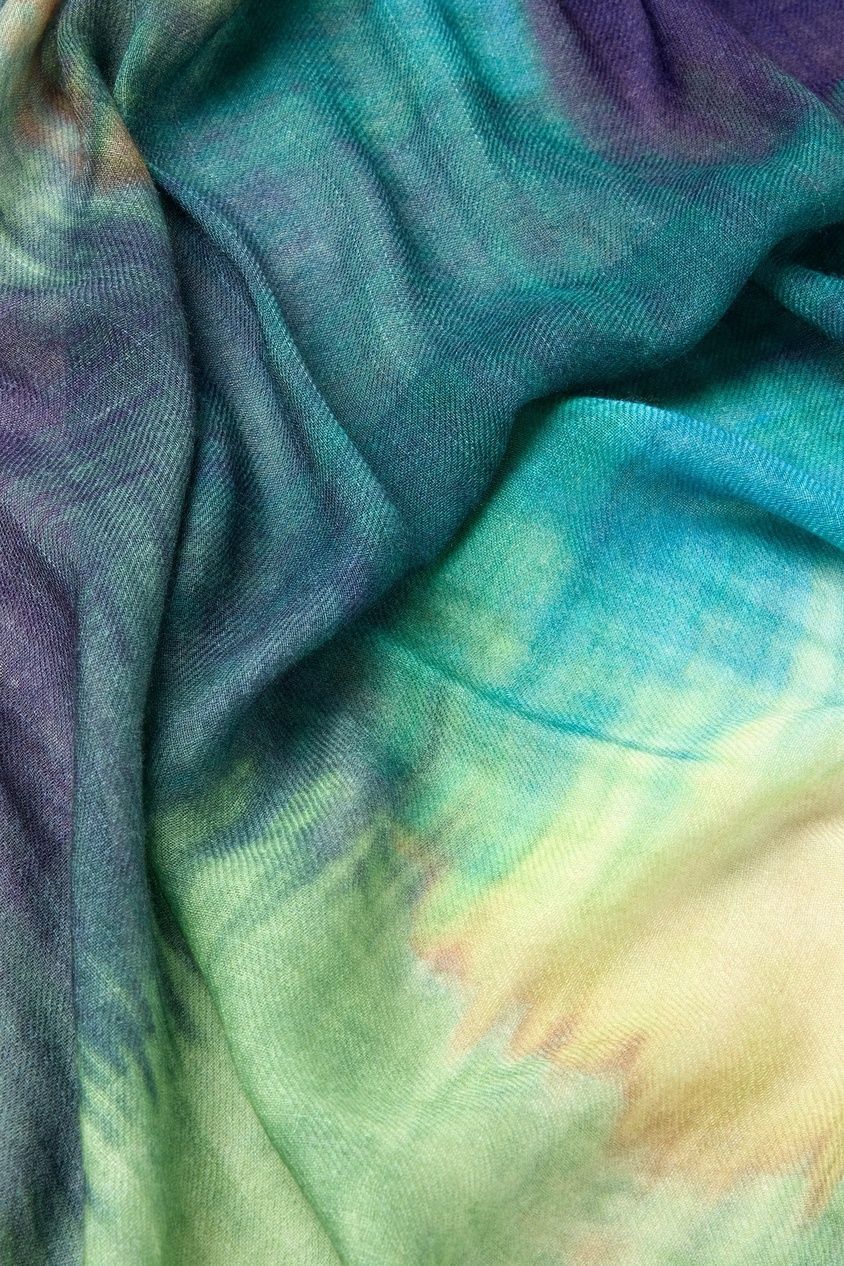 A detailed close-up of the Colour Blend Circle Print Scarf unveils its sumptuously soft, tie-dyed fabric with a watercolor-inspired design that beautifully merges shades of blue, green, and yellow.