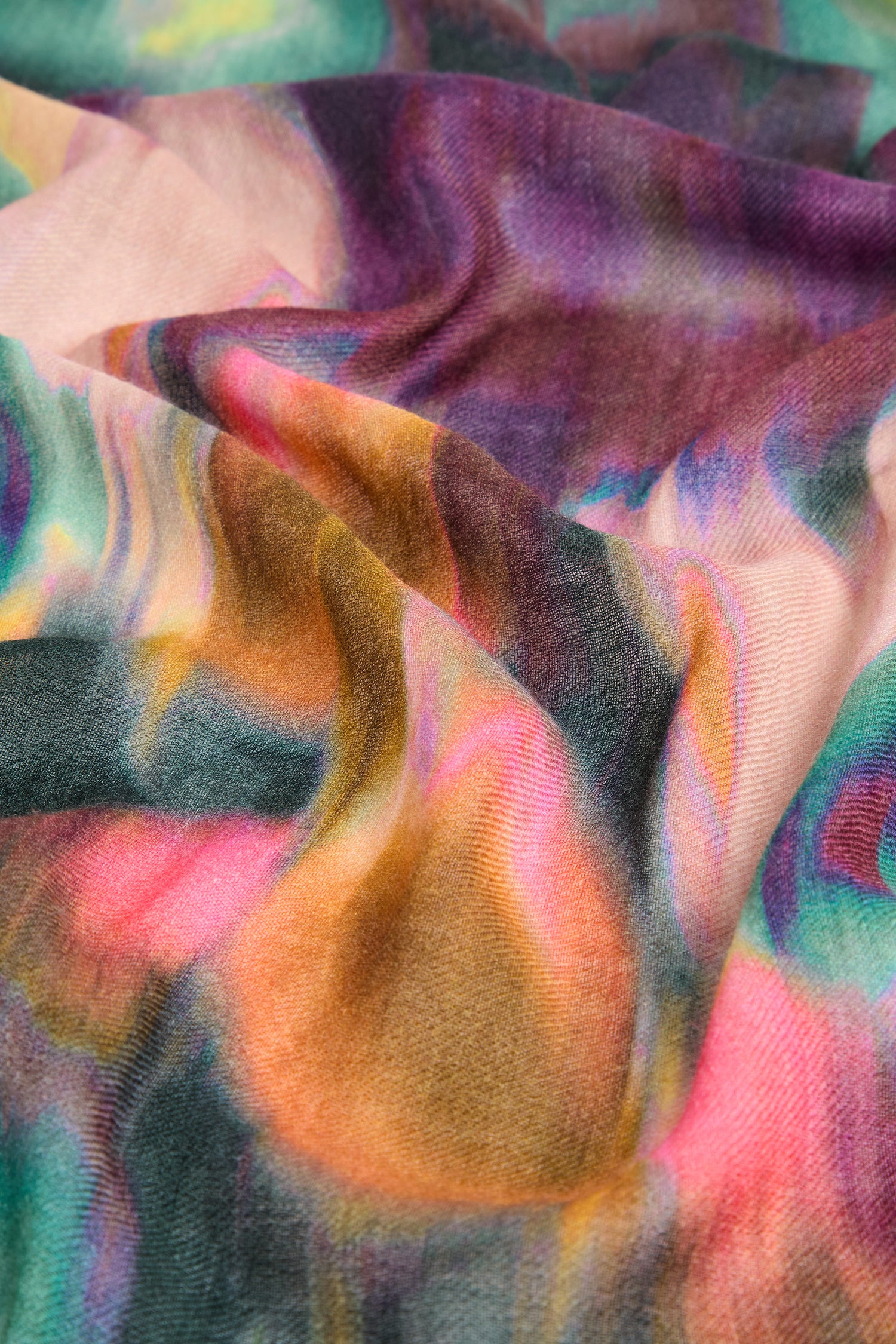 Close-up of the Colour Fusion Wool Mix Scarf, showcasing its crumpled, multi-colored fabric with a watercolor print tie-dye pattern in jewel-tone shades of pink, orange, green, and purple.