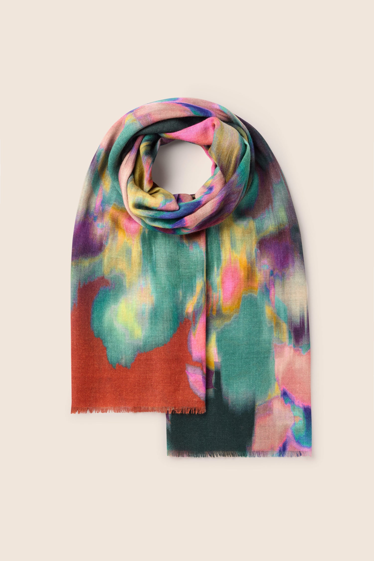 The Colour Fusion Wool Mix Scarf, with its vibrant jewel-tone colors in shades of green, pink, orange, and purple arranged in a watercolor-like design, is folded and laid flat against a beige background. This scarf beautifully showcases its colorful artistry.