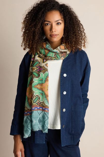 A person with curly hair wearing a blue jacket and a Mosaic Print Wool Mix Scarf stands against a plain background, looking directly at the camera.