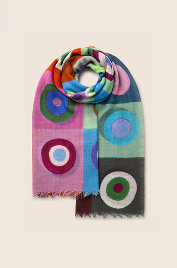 The Concentric Circles Wool Scarf features a multicolored design with bold concentric circles in shades of pink, blue, green, and orange set against a plain background. This geometric print accessory injects vibrant energy into any outfit.