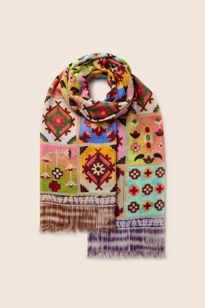 A vibrant Patchwork Print Wool Scarf showcasing intricate geometric and floral patterns, complete with fringe ends, is displayed against a beige background. This stylish accessory, rich in colorful designs, is perfect for enhancing any outfit.