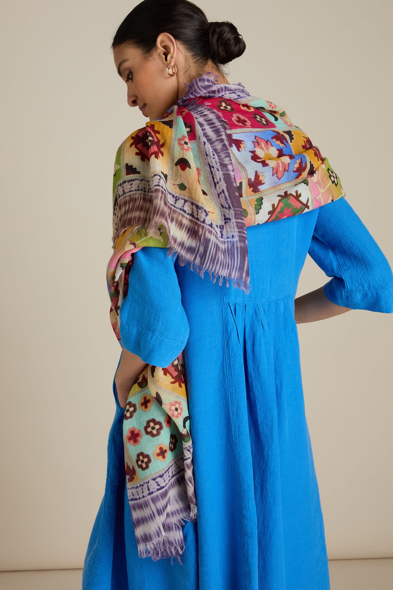 A person wearing a blue dress is seen from the back. They have short hair tied up and are draped with an all-occasion styling, Patchwork Print Wool Scarf over their shoulder.