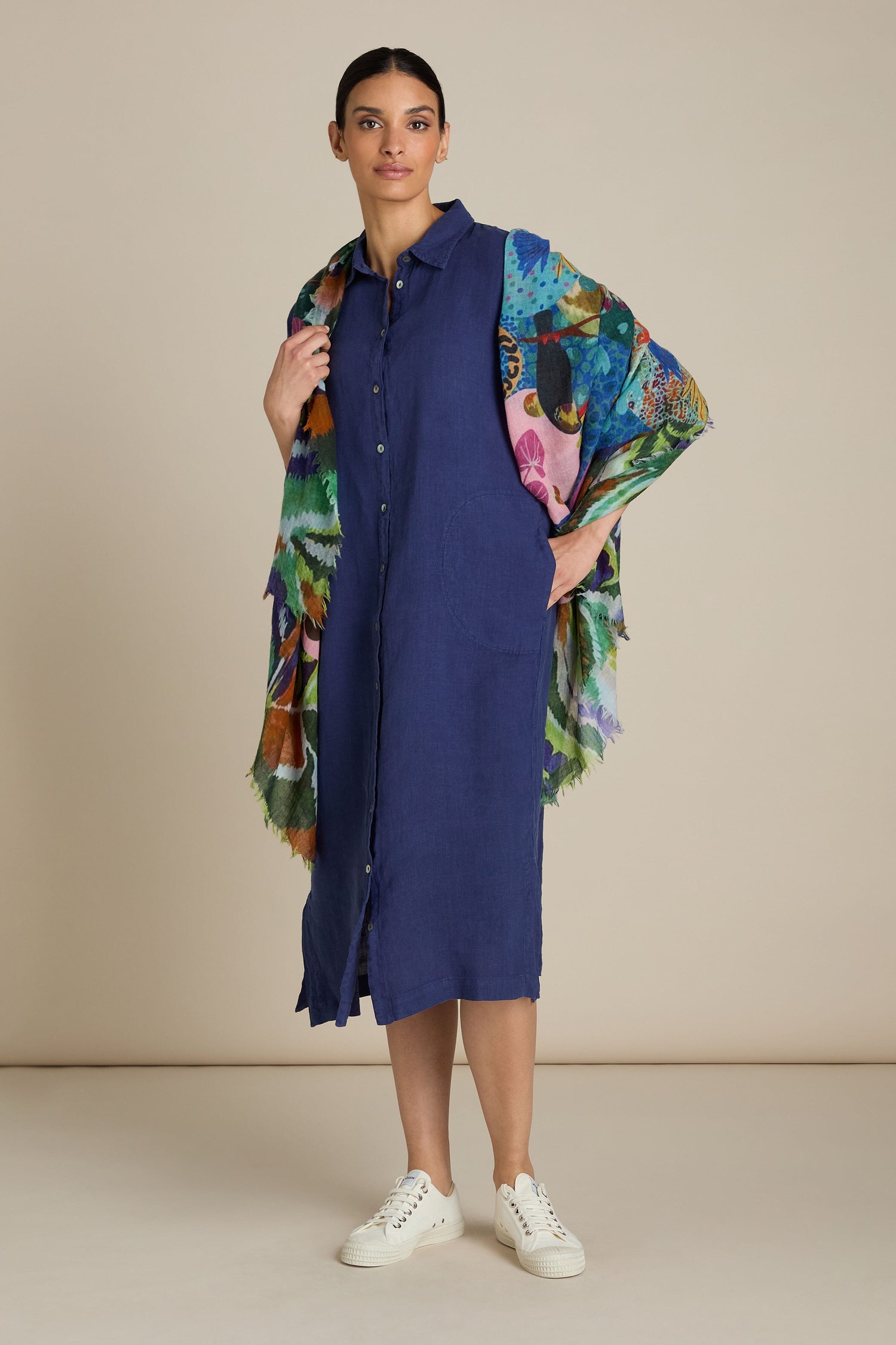 A person stands against a plain background wearing a blue buttoned dress, white sneakers, and the versatile Jungle Print Wool Scarf for all-occasion styling.