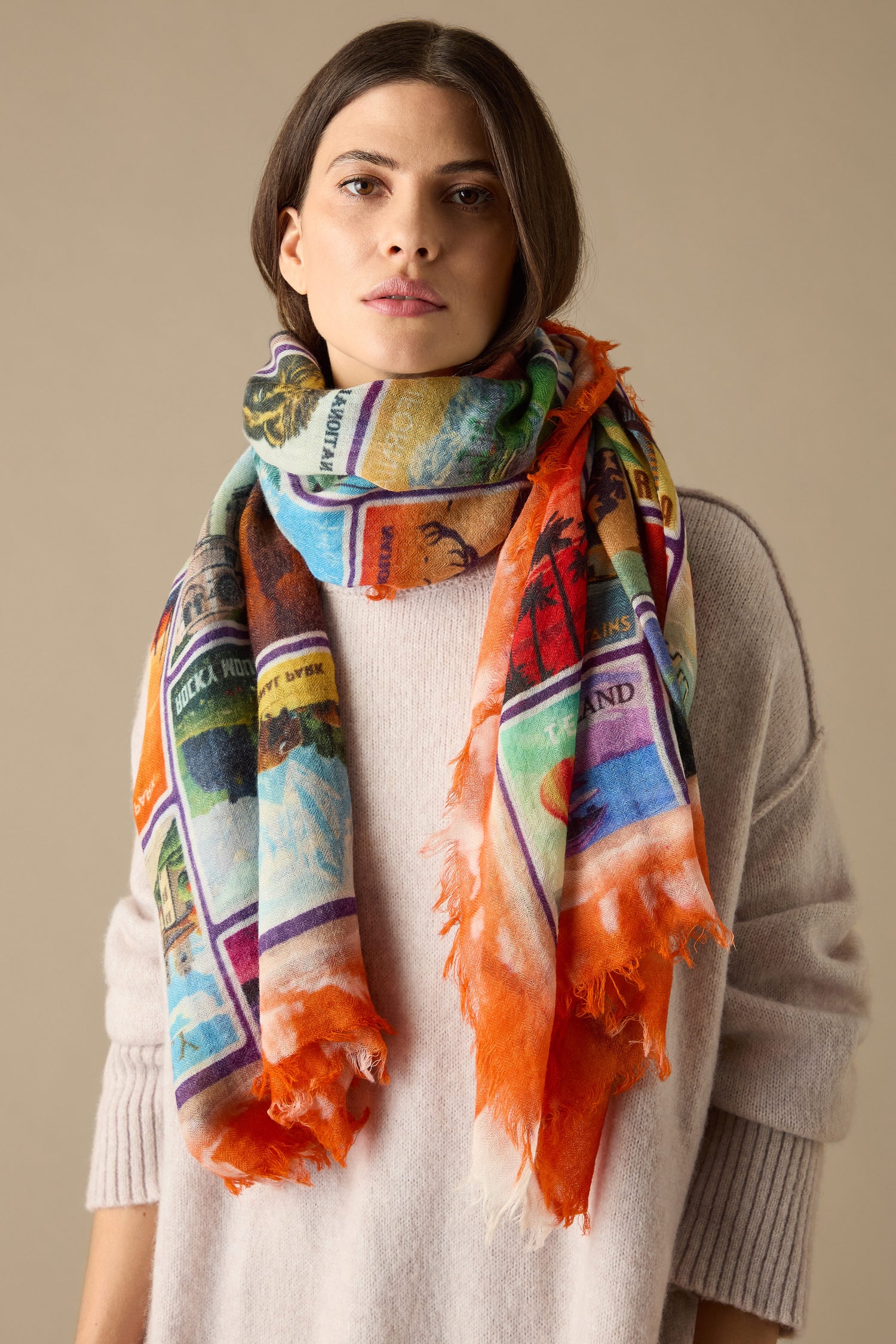 A person draped in the "Postcards From Around the World" wool scarf, its graphic prints evoking a sense of wanderlust, complements their light sweater against a neutral background.