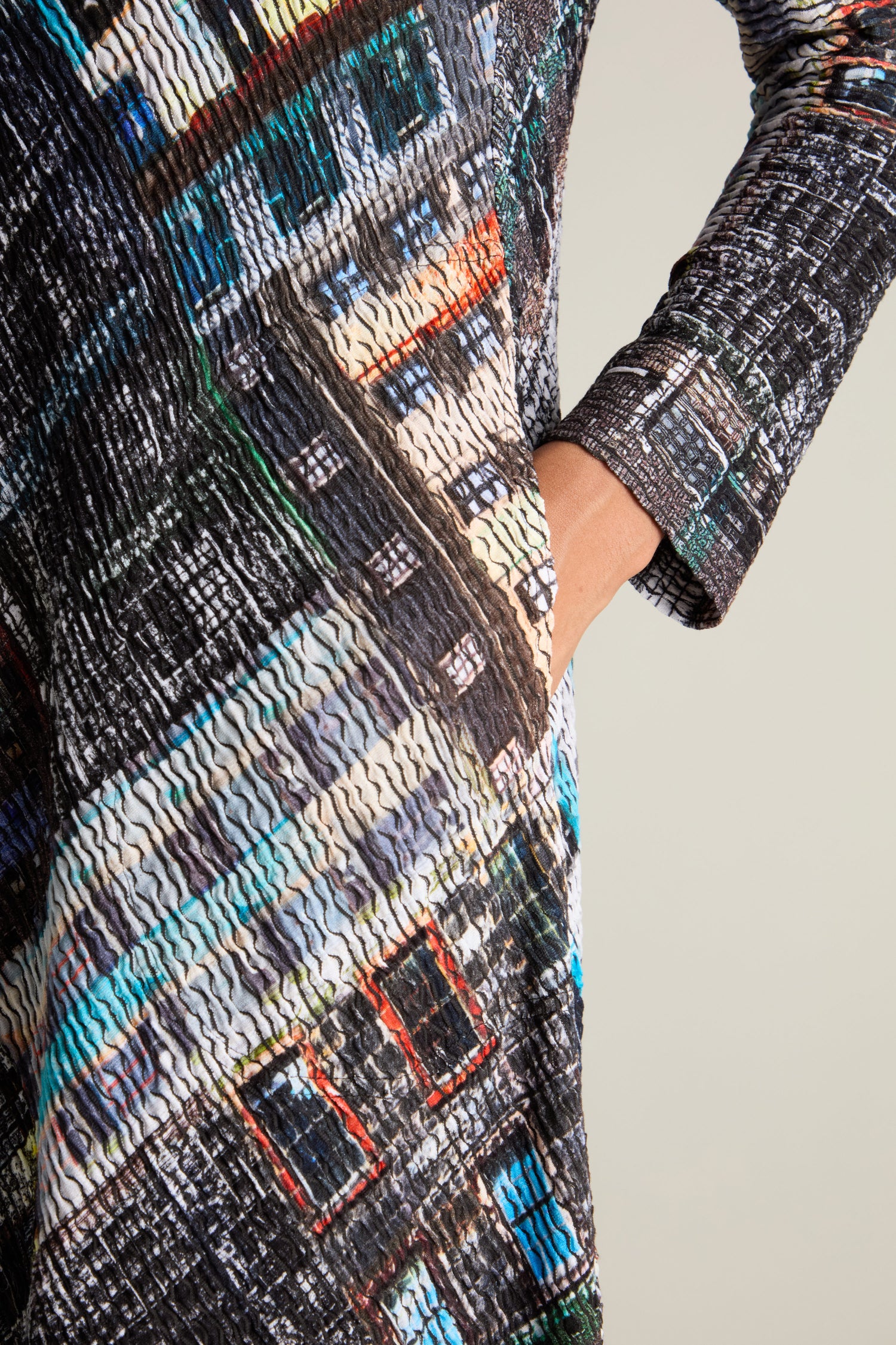 A close-up of a person's torso wearing the Ramona Facade Print Jersey Dress with one hand in their pocket against a plain background, showcasing its textured, multicolored pattern and elegant House facade design.