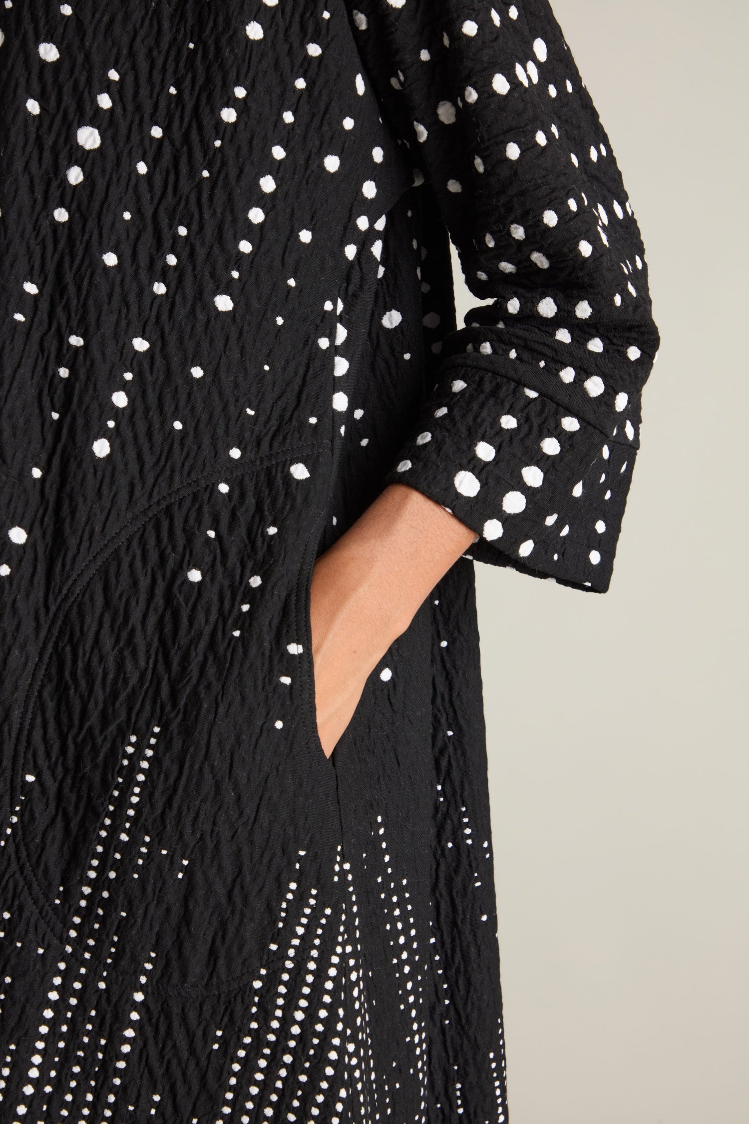 A person wearing the Tiffany Multi Size Spot Jersey Dress, crafted from premium black jersey fabric adorned with white dotted patterns, with one hand placed in a pocket.