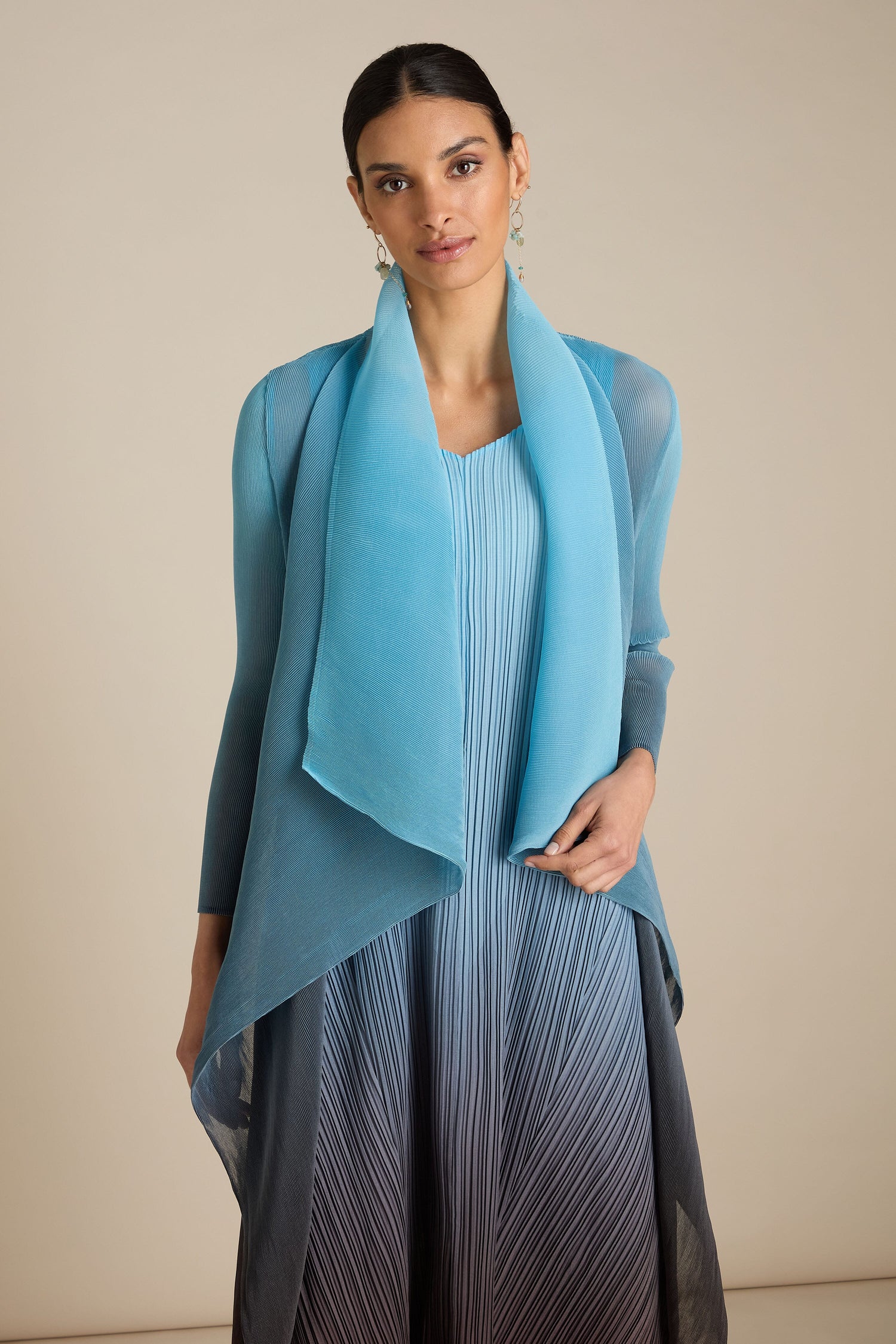 A person dons a light blue dress paired with a matching sheer overlay cardigan, enhanced by a handcrafted Pleated Jacket inspired by Japanese craft, while posing against a neutral background.