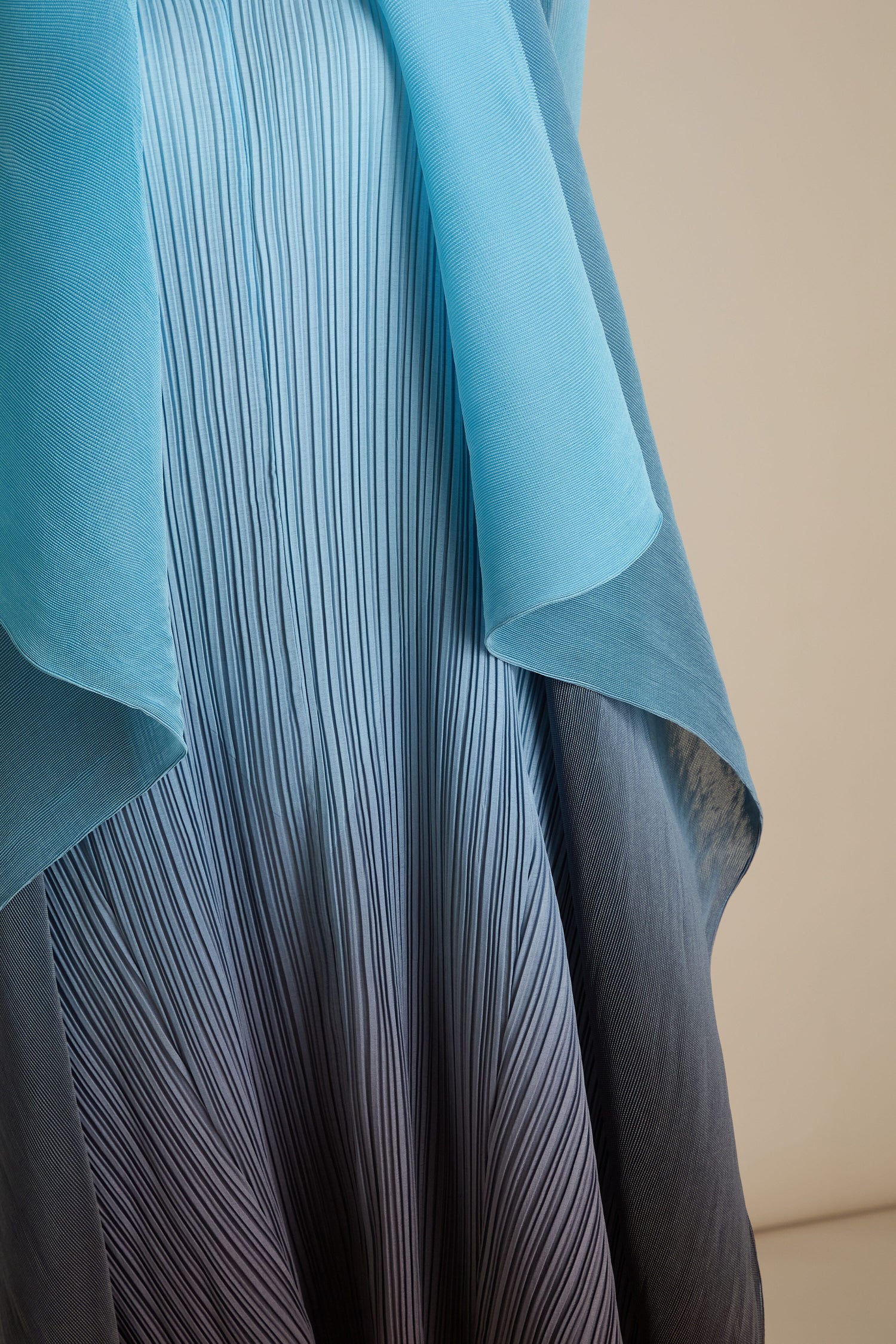 A close-up of a pleated light blue and navy Pleated Jacket with a layer of sheer fabric draped over it, showcasing the intricate beauty inspired by Japanese craft.