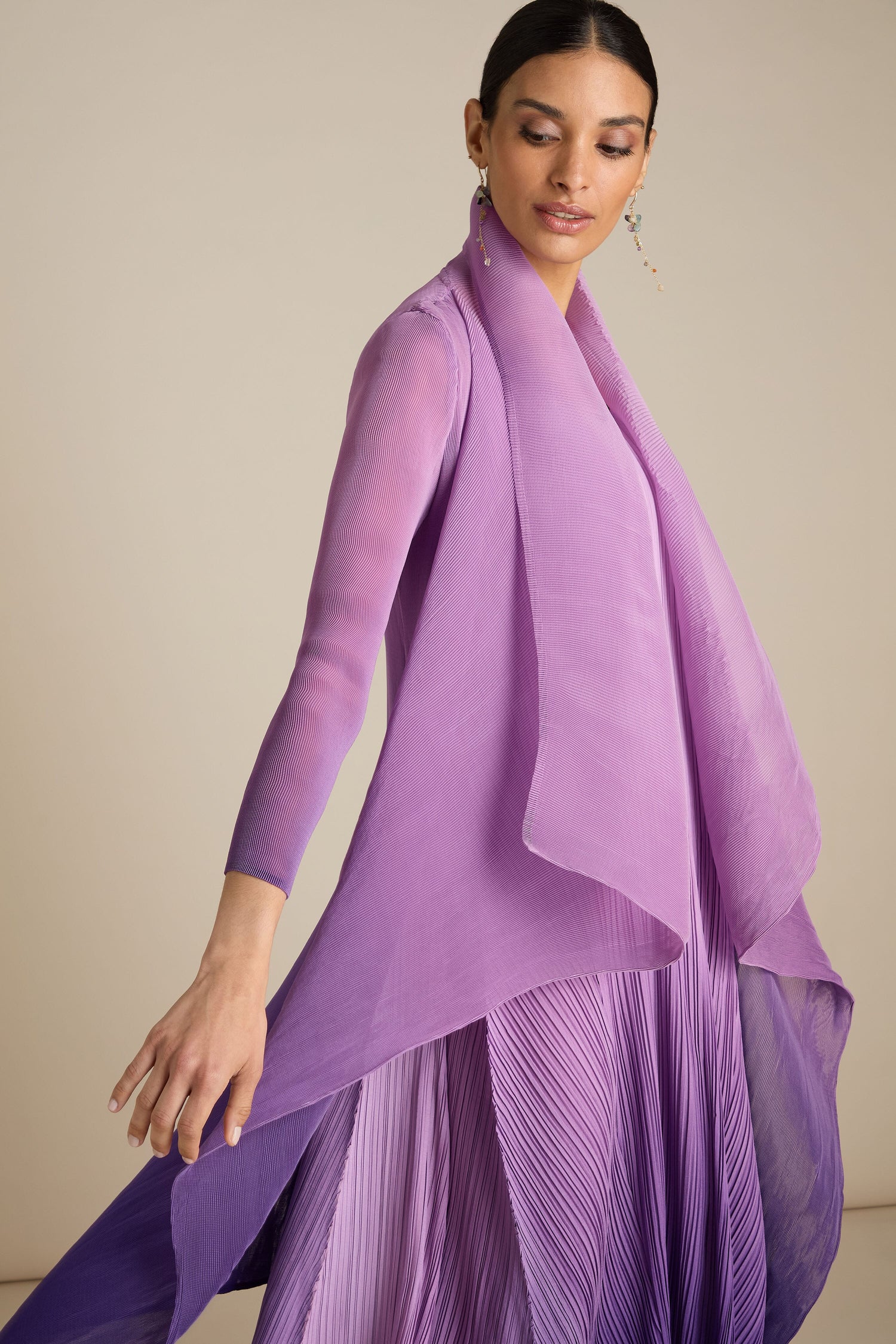 A person wearing a layered, flowing, semi-transparent purple outfit that includes the Pleated Jacket and a pleated skirt crafted with Japanese precision poses gracefully.