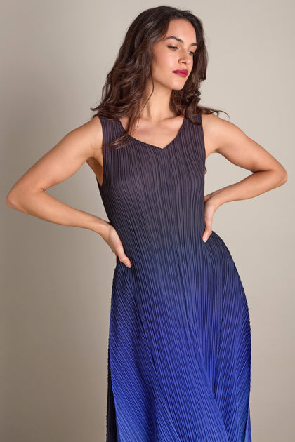 A person stands confidently in a Pleated Dress, its detailed pleated fabric forming an elegant gradient from black to blue, hands resting on their hips.