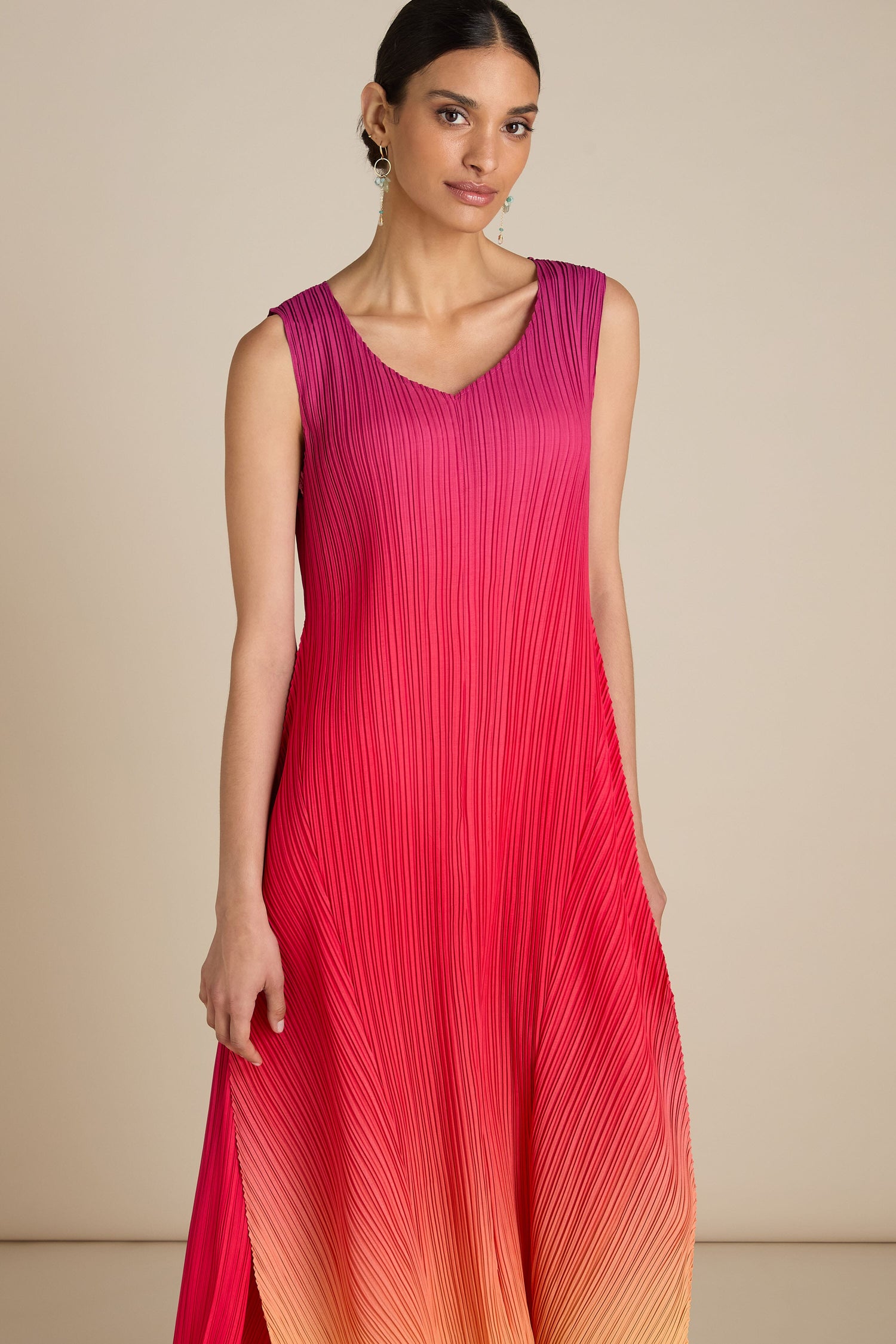 Person wearing the Pleated Dress, a sleeveless garment with a gradient design in shades of pink, red, and orange that exudes bohemian flair, standing against a neutral background.