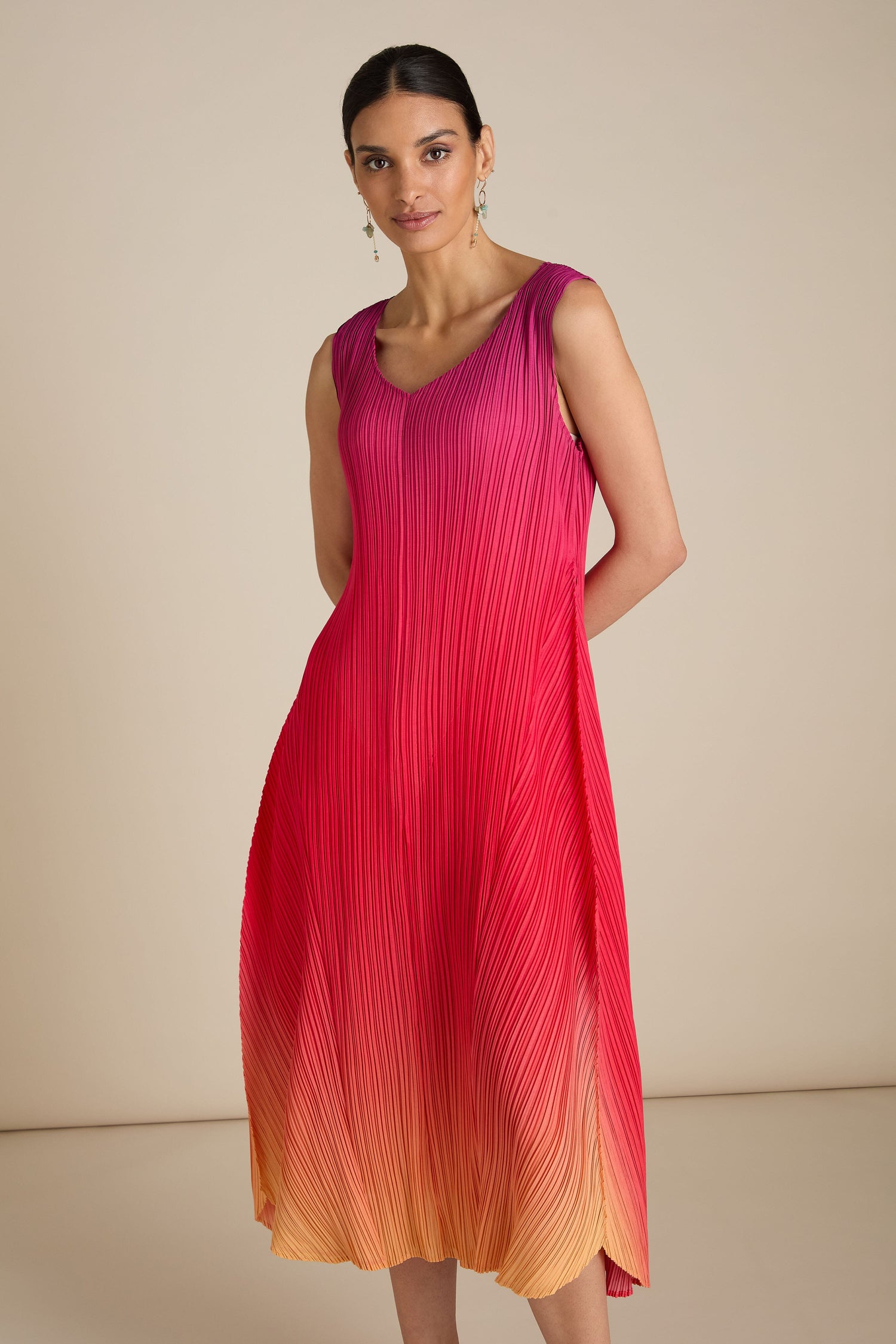 Person wearing a sleeveless Pleated Dress with a relaxed silhouette, showcasing a gradient transition from magenta at the top to orange at the bottom, posing against a plain background.