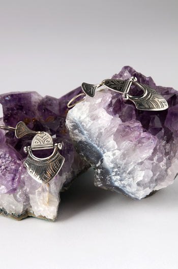 The Engraved Silver Tuareg Earrings, part of a unique jewellery collection, are elegantly displayed on purple amethyst crystal clusters against a gray background.