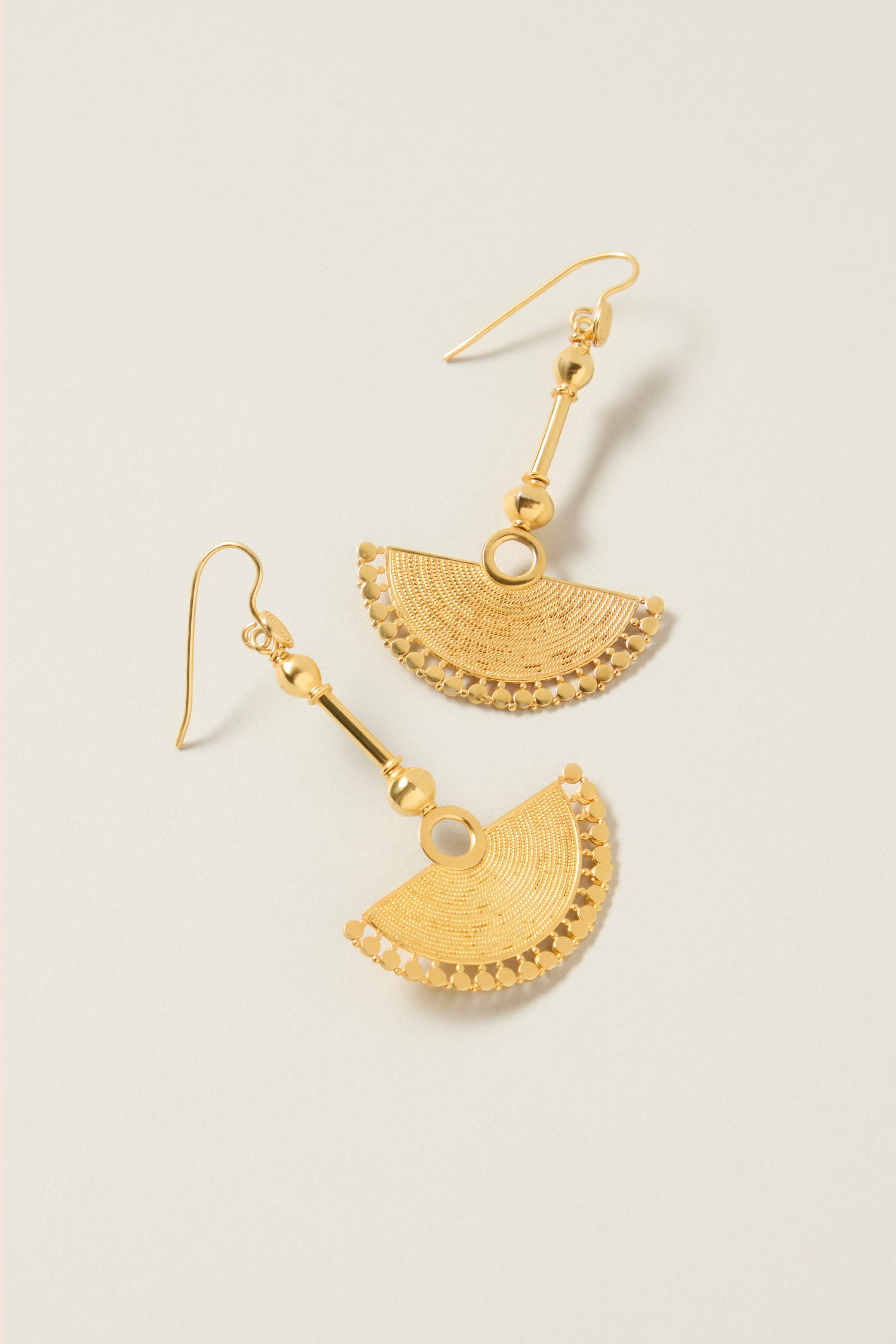 A pair of 18ct Gold Vermeil Fan Earrings, showcasing semi-circular, fan-like pendants with spherical embellishments that exude bohemian elegance, rests on a light-colored surface.