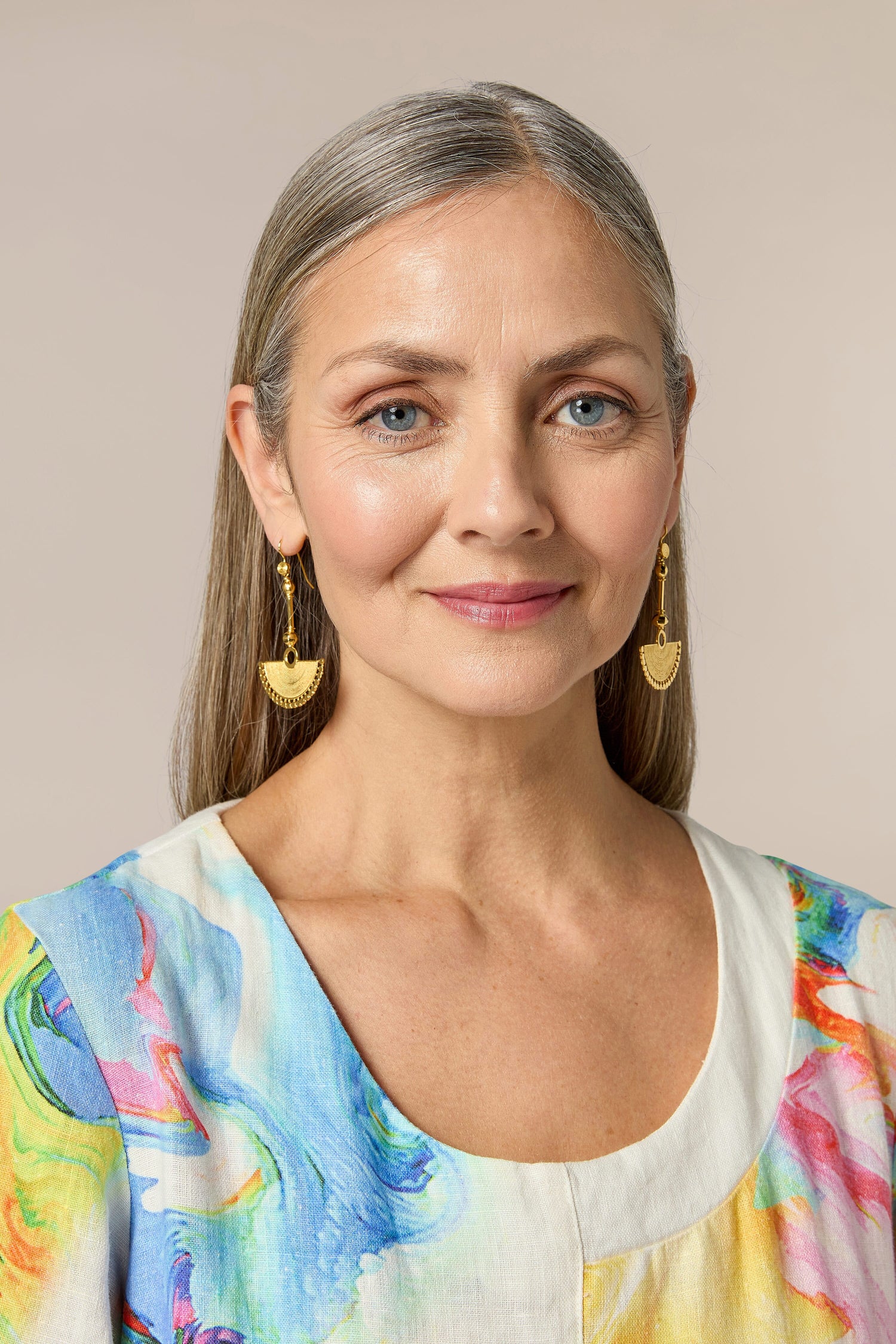 A woman wearing Gold Vermeil Fan Earrings and a colorful top with a bohemian flair.