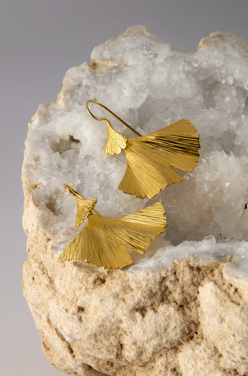 Gold Vermeil Ginkgo Leaf Earrings grace a white textured stone, epitomizing nature-inspired elegance with their exquisite design.