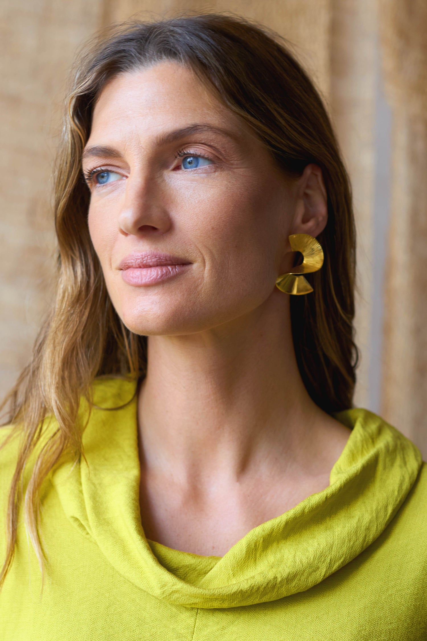 Wearing a lime green top and Gold Vermeil Twist Earrings, a person with long hair glances to the side.