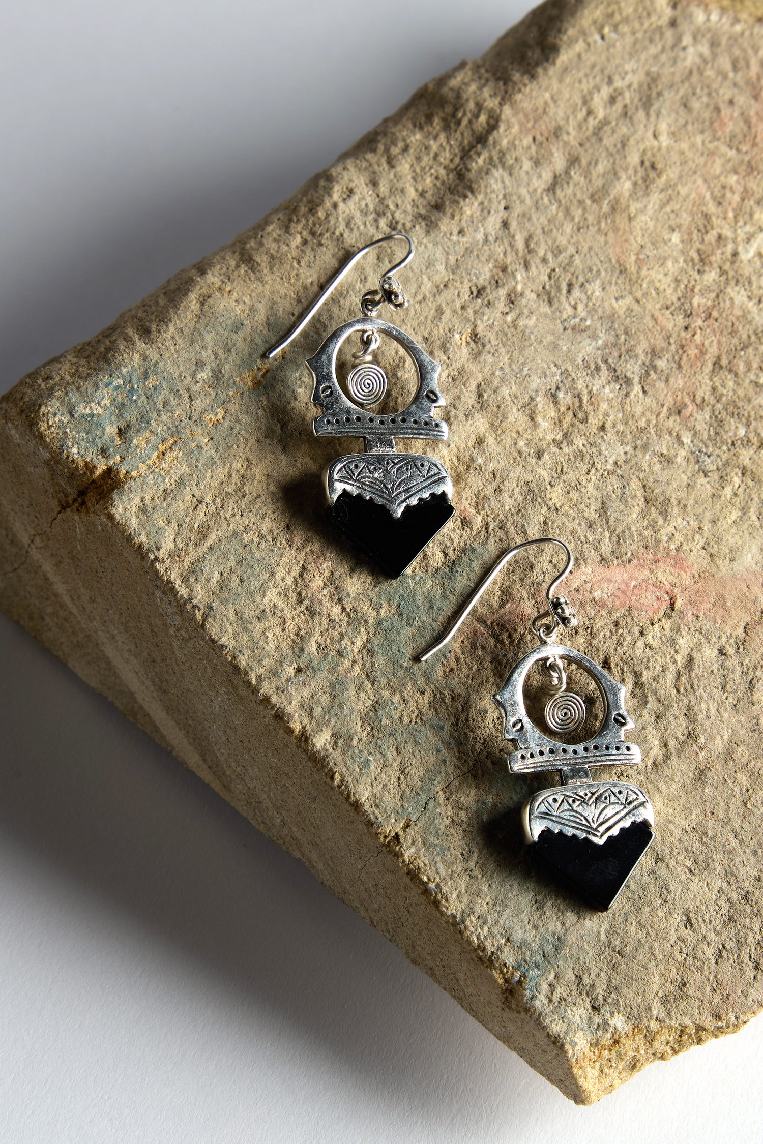 The Silver and Black Onyx Tuareg Earrings, featuring intricate designs, are elegantly displayed on a textured stone surface.