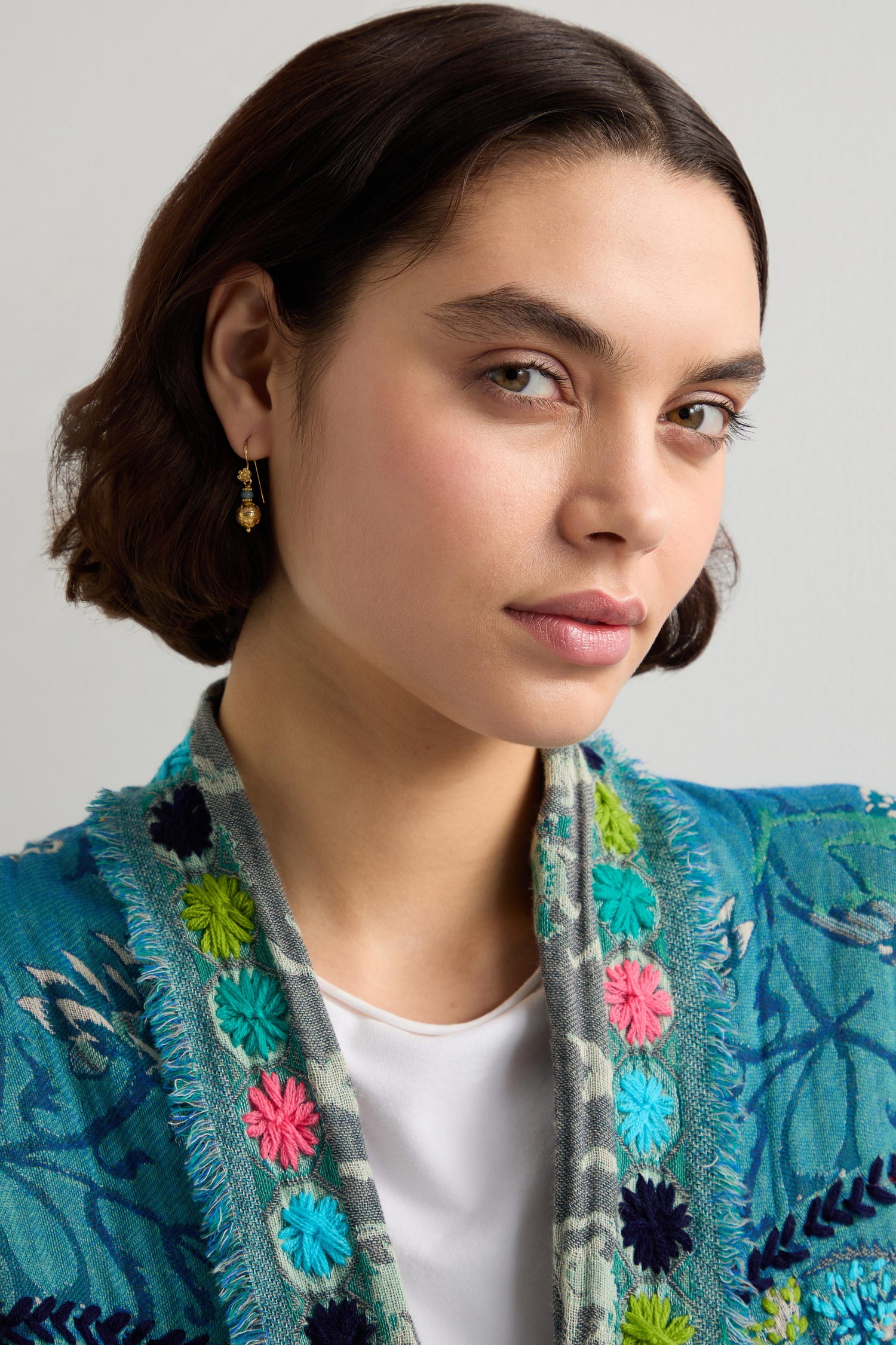 A person with short brown hair, wearing a blue embroidered jacket and Gold Vermeil Amazonite Bead Earrings, looks towards the camera.