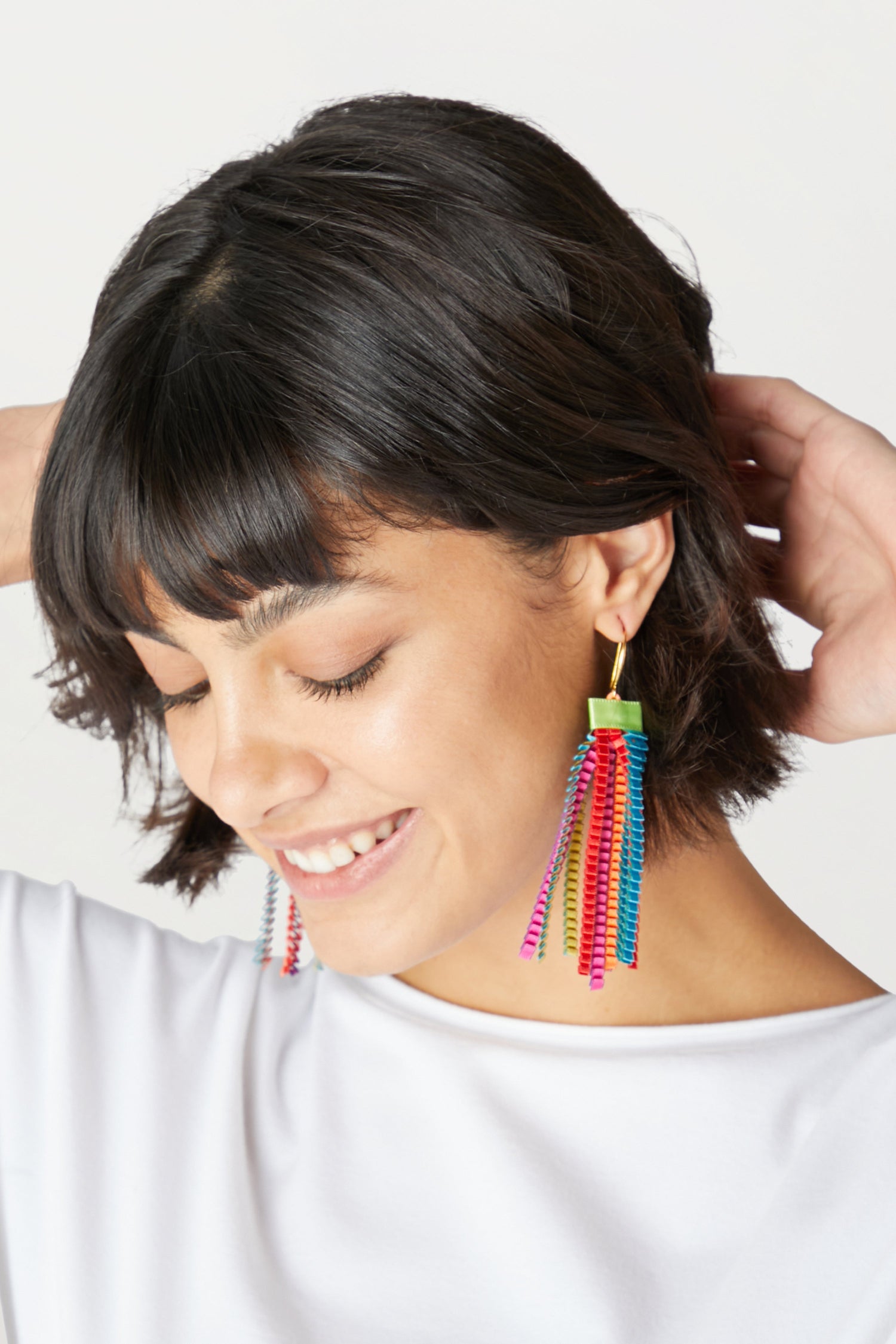 A woman wearing vibrant Pleated Earrings adorned with colorful tassels made from synthetic-silk.