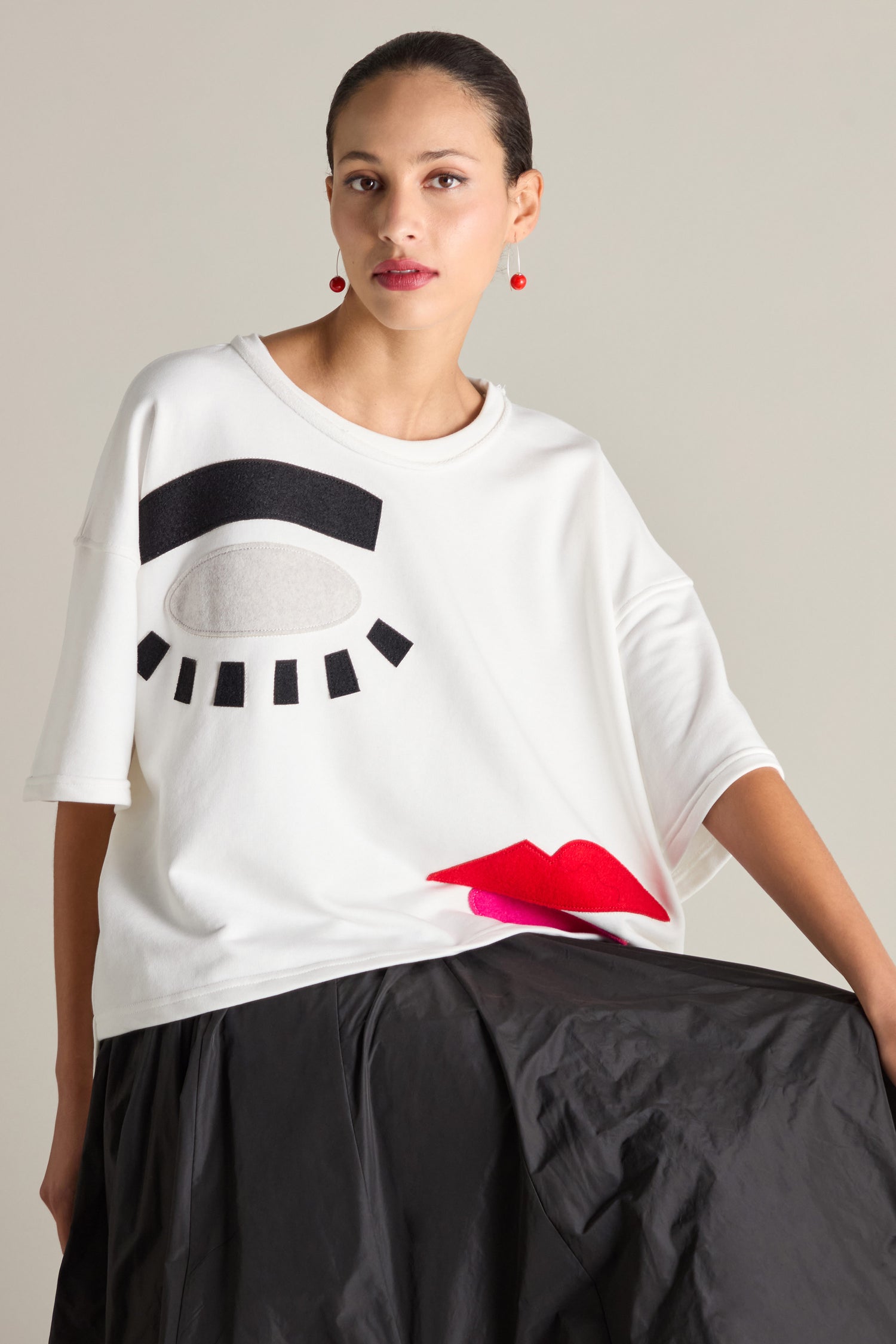 A person wearing the Eyes And Lips Jersey Top, featuring a white shirt with an abstract black and red graphic eye motif, and a black skirt, posing against a plain background.