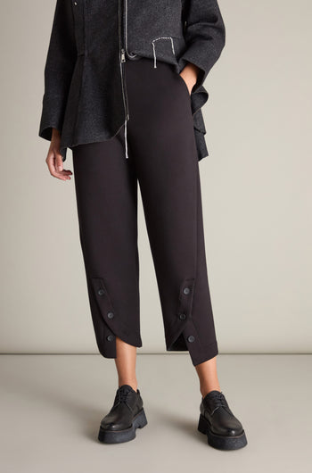 A person is wearing a dark grey long-sleeve top, Button Detail Trousers in black, and black platform shoes, standing against a plain background. The outfit creates a dynamic silhouette, making each element in this ensemble feel like a statement piece.