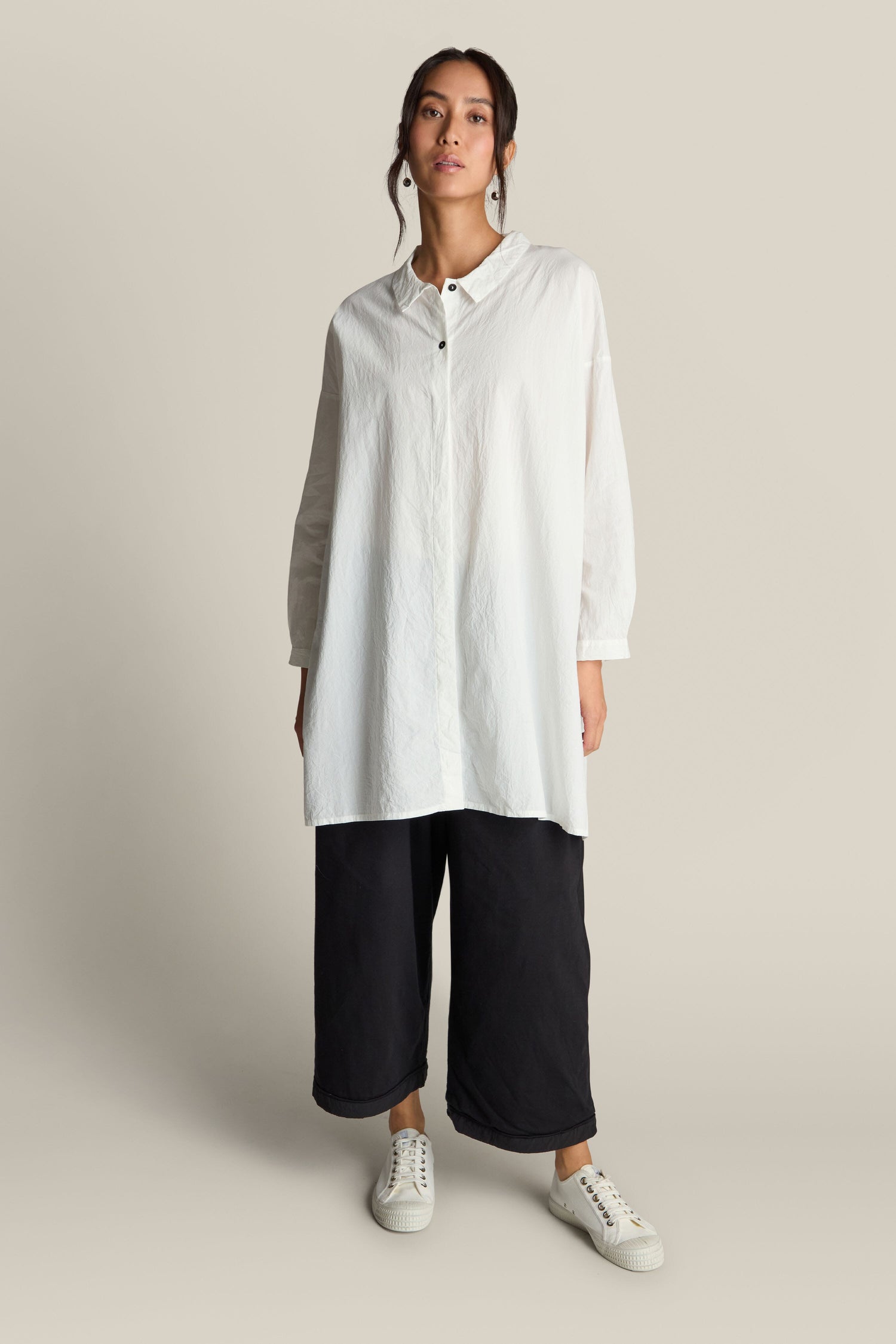 An individual is stylishly attired in an Oversize Shirt made of premium cotton, paired with loose black pants and white sneakers, effortlessly exuding an air of relaxed sophistication.